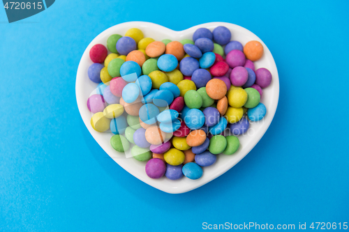 Image of candies on heart shaped plate over blue background