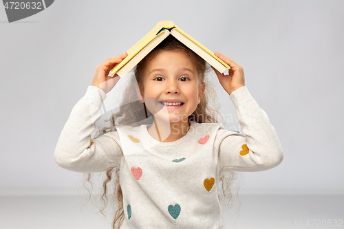 Image of portrait of smiling girl with book on head