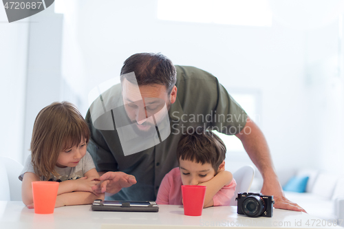 Image of single father at home with two kids playing games on tablet