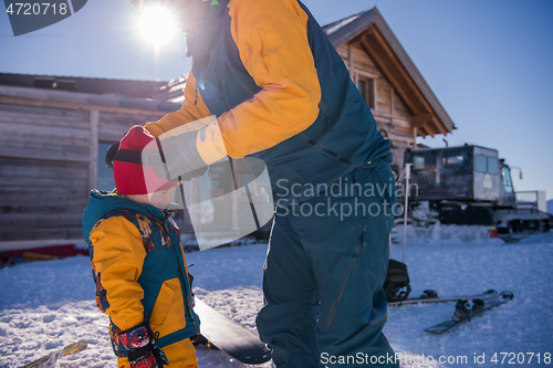 Image of father preparing his little son for the first time on a snowboar