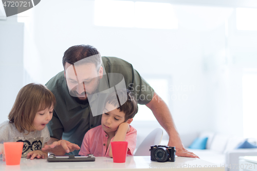 Image of single father at home with two kids playing games on tablet