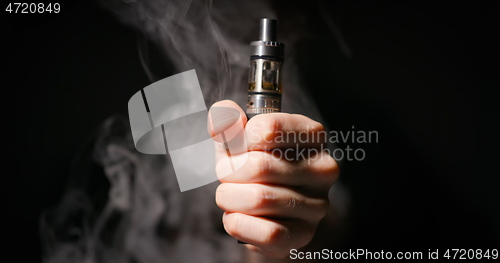 Image of Electronic cigarette grabbed by male hand against dark background and vapor