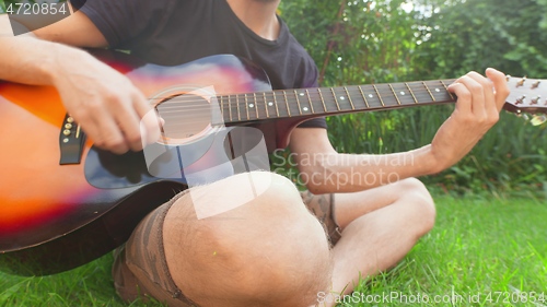 Image of Man sitting in the grass playing guitar