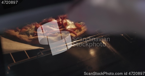 Image of Homemade pizza being checked on in oven