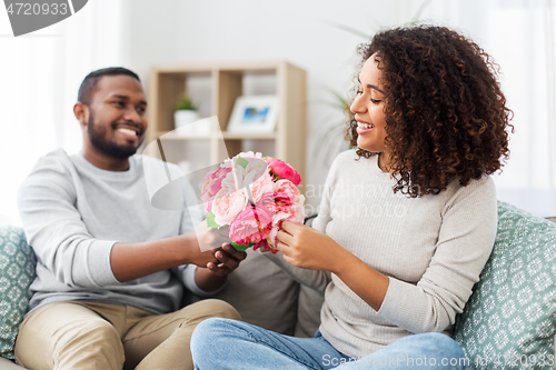 Image of happy couple with bunch of flowers at home