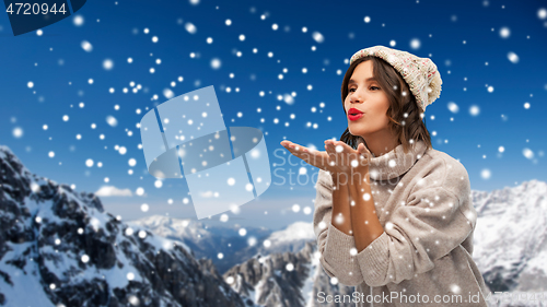 Image of young woman in knitted winter hat sending air kiss