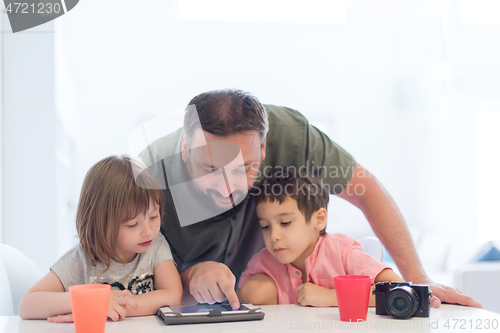 Image of single father at home with two kids playing games on tablet