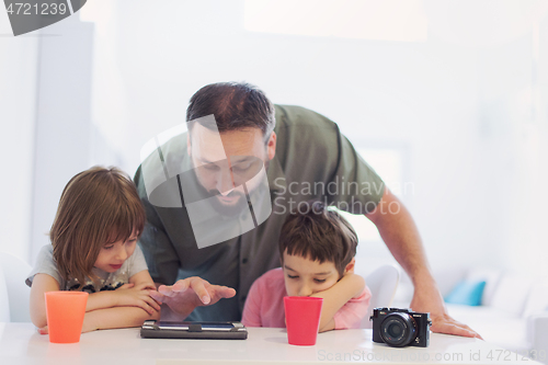 Image of single father at home with two kids playing games on tablet