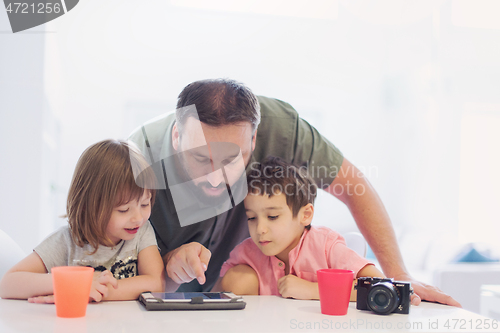 Image of single father at home with two kids playing games on tablet