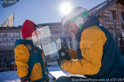 Image of father preparing his little son for the first time on a snowboar