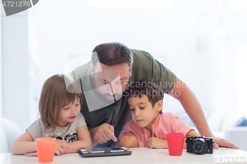 Image of single father at home with two kids playing games on tablet