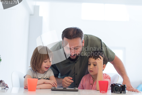 Image of single father at home with two kids playing games on tablet