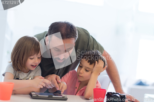 Image of single father at home with two kids playing games on tablet