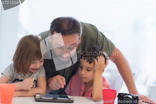 Image of single father at home with two kids playing games on tablet