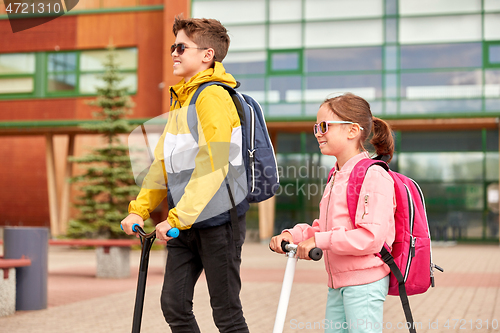 Image of happy school children with backpacks and scooters