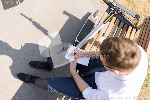 Image of smiling businessman writing to notebook in city