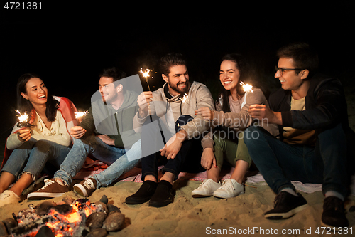 Image of happy friends with sparklers at camp fire at night