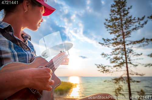 Image of Woman at sunset playing the ukulele