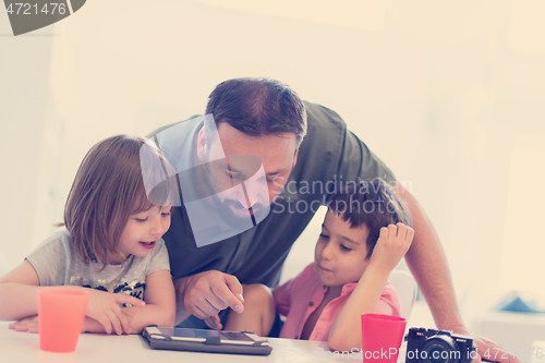 Image of single father at home with two kids playing games on tablet