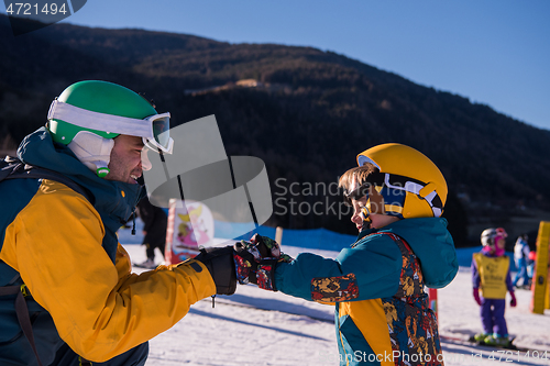 Image of father preparing his little son for the first time on a snowboar