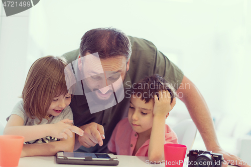 Image of single father at home with two kids playing games on tablet