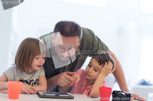 Image of single father at home with two kids playing games on tablet