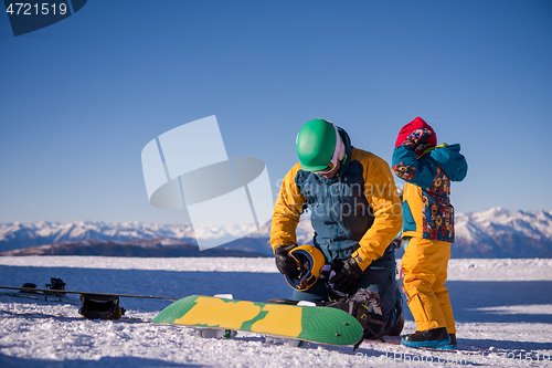 Image of father preparing his little son for the first time on a snowboar