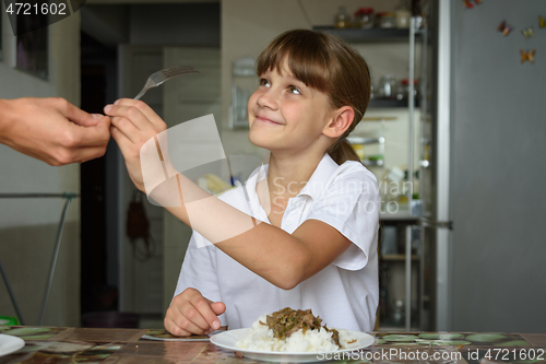 Image of A girl takes a fork from her mother\'s hand while preparing to dine at the kitchen table