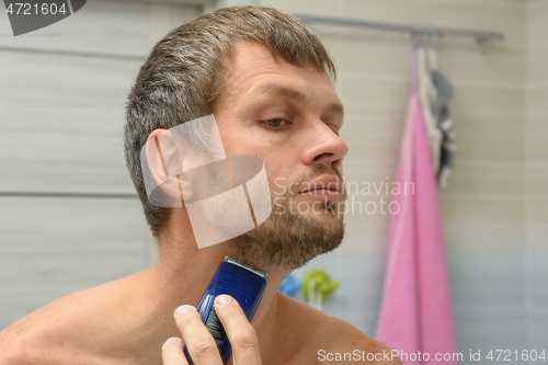 Image of A man smooths his beard on his face with a hair clipper