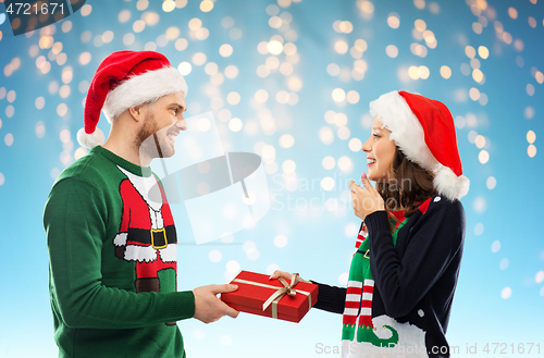 Image of happy couple in christmas sweaters with gift box