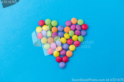 Image of candy drops in shape of heart on blue background