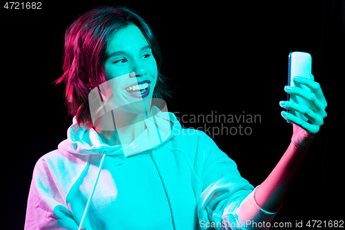 Image of woman taking selfie by smartphone in neon lights