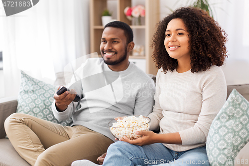 Image of african couple with popcorn watching tv at home