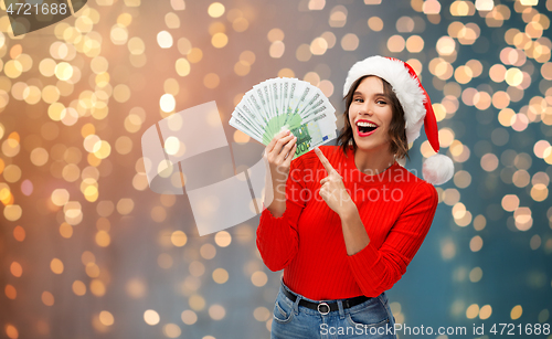 Image of happy woman in santa hat with money on christmas