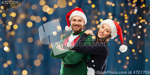 Image of happy couple in christmas sweaters and santa hats