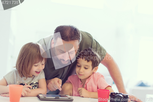 Image of single father at home with two kids playing games on tablet