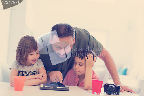 Image of single father at home with two kids playing games on tablet