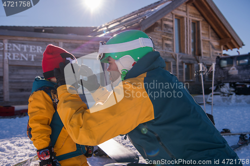 Image of father preparing his little son for the first time on a snowboar