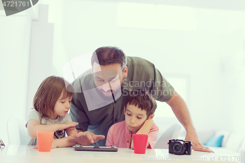 Image of single father at home with two kids playing games on tablet