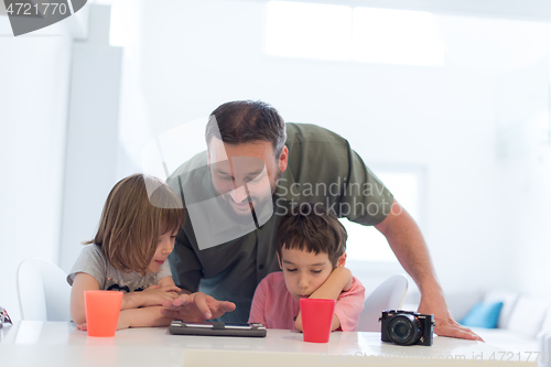 Image of single father at home with two kids playing games on tablet