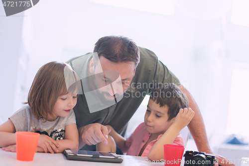 Image of single father at home with two kids playing games on tablet