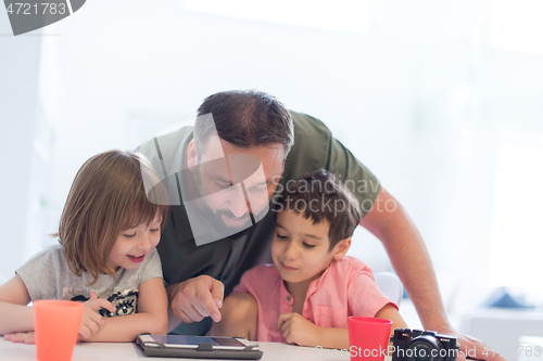 Image of single father at home with two kids playing games on tablet