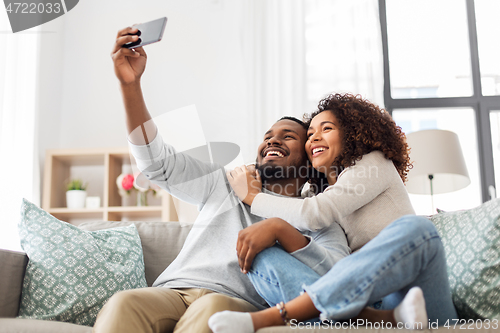 Image of happy couple with smartphone taking selfie at home