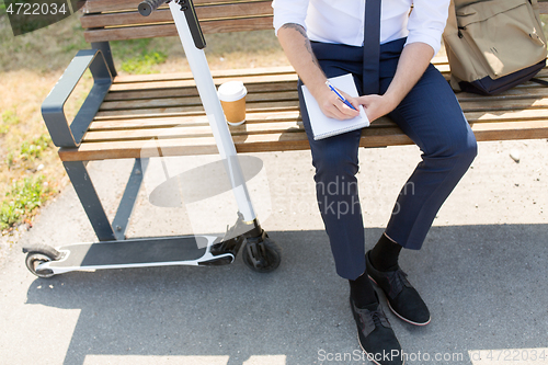 Image of smiling businessman writing to notebook in city