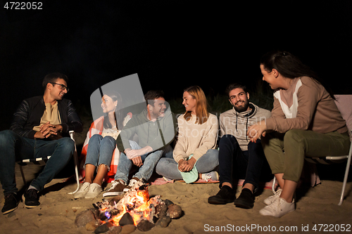 Image of group of friends sitting at camp fire on beach