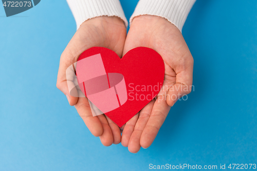 Image of hands holding red heart shape on blue background