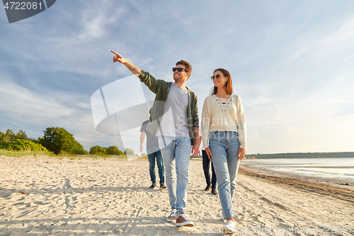 Image of happy friends walking along summer beach