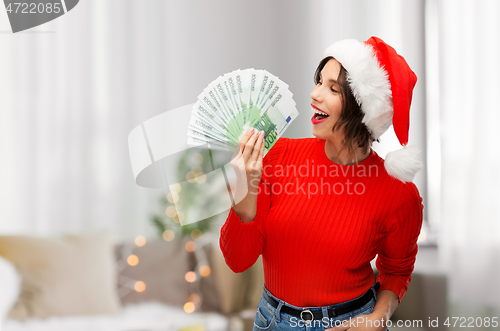 Image of happy woman in santa hat with money on christmas