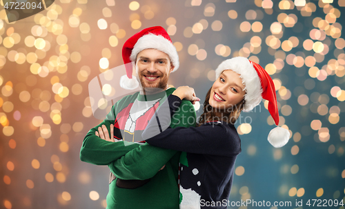 Image of happy couple in christmas sweaters and santa hats