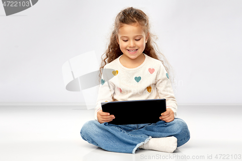 Image of smiling girl with tablet computer sitting on floor